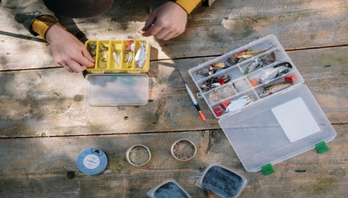 Person organizing Bass fishing baits in plastic tackle organizers on a wooden picnic table