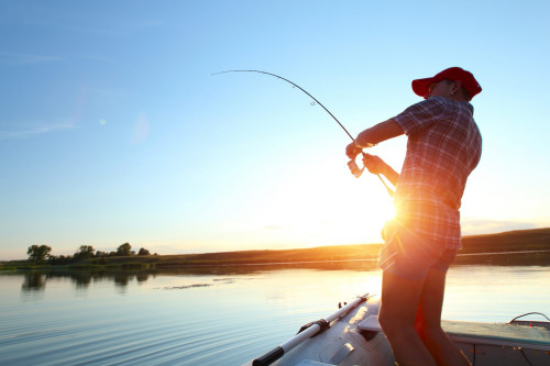 Man fishing off boat on a lake with sunset