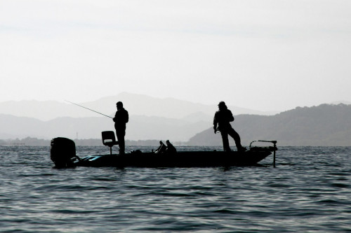 Two people standing on fishing boat in middle of lake fishing
