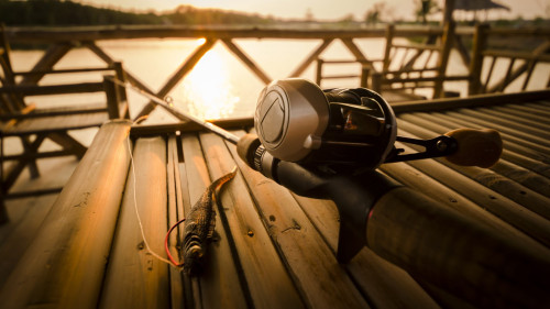 Fishing reel and lure sitting on a dock table with sunset
